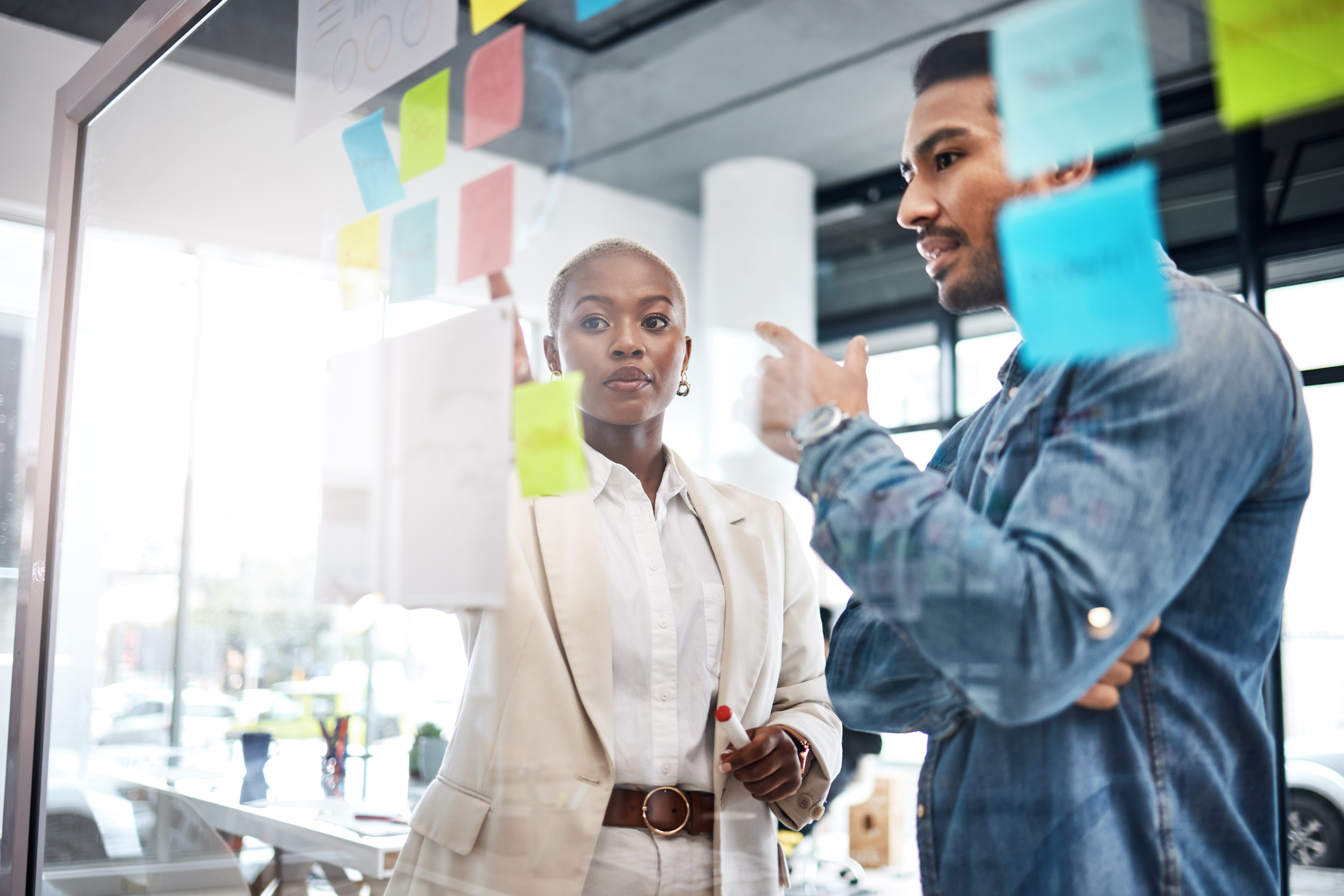 Two professionals collaborating at a glass wall covered in sticky notes